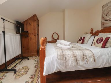 A bedroom with a wooden bed with white bedding and floral pillows a wooden wardrobe a dressing table and a rug on wooden floor at Ty  Llewelyn in Capel Curig near Betws-Y-Coed