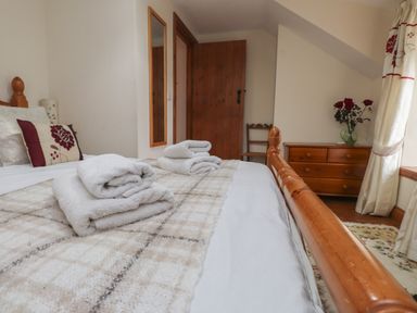 A bedroom with a wooden bed and dresser a mirror on the wall and towels on the bed at Ty Llewelyn in Capel Curig near Betws Y Coed