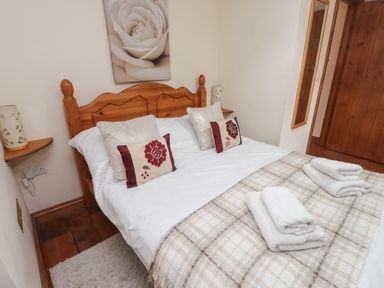 A bedroom with a wooden bed frame cushions folded towels and a plaid blanket at Ty Llewelyn Capel Curig near Betws-Y-Coed