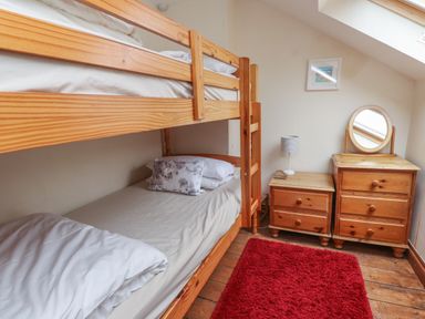 A bedroom with wooden bunk beds a red rug a wooden chest of drawers with a round mirror and a bedside table with a lamp at Ty  Llewelyn in Capel Curig near Betws-Y-Coed