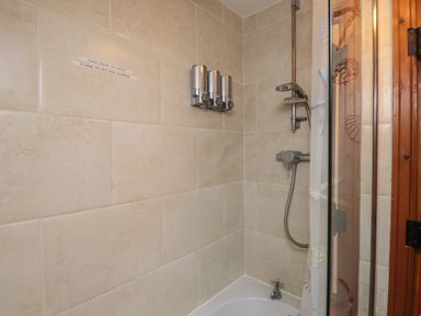A shower area with beige tiled walls, a showerhead, soap dispensers, a bathtub, and a shower curtain at Ty  Llewelyn in Capel Curig near Betws-Y-Coed