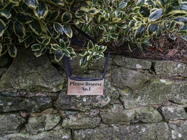 A stone wall with a wooden sign reading Please Reserve No 1 hanging among green and yellow leaves at 1 Boarbank Farm Allithwaite near Cartmel