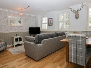 A living room with a gray sofa a television a dining table with plaid chairs and a mounted deer head at 1 Boarbank Farm in Allithwaite near Cartmel