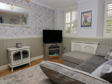 A sitting room with a television on a stand a gray sofa a white heater cover and a mirror on the wall at 1 Boarbank Farm in Allithwaite near Cartmel