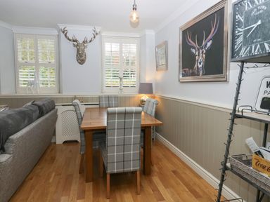 A dining area with a wooden table and plaid chairs near windows with shutters and deer decorations at 1 Boarbank Farm Allithwaite near Cartmel