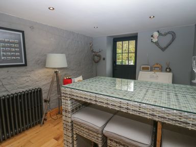 A room with a wicker table and stools a tripod floor lamp a radiator a framed picture and a door at 1 Boarbank Farm in Allithwaite near Cartmel