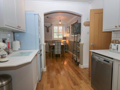 A kitchen with white cabinets and appliances leading to a dining area with a wooden table and plaid chairs at 1 Boarbank Farm in Allithwaite near Cartmel