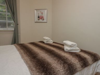 A bed with a brown blanket and two sets of folded white towels in a room with a window and a framed picture on the wall at 1 Boarbank Farm in Allithwaite near Cartmel