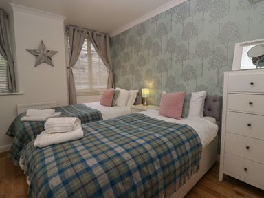 A bedroom with two single beds with plaid blankets and pillows next to a white dresser at 1 Boarbank Farm in Allithwaite near Cartmel
