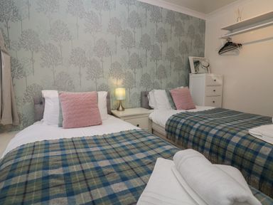 A bedroom with two single beds with plaid blankets and a nightstand with a lamp at 1 Boarbank Farm in Allithwaite near Cartmel