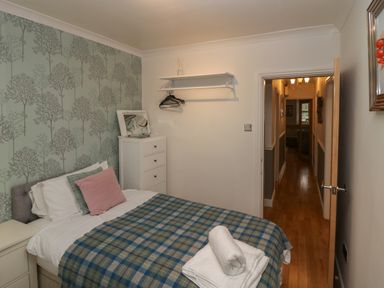 A bedroom with a bed covered with a plaid blanket and stacked towels near a dresser and an open door showing a hallway at 1 Boarbank Farm in Allithwaite near Cartmel