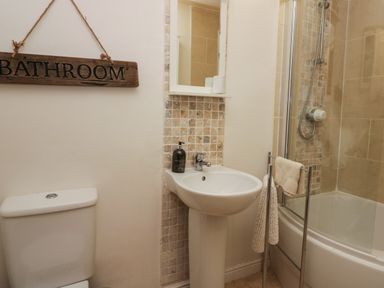A bathroom with a toilet sink mirror and bathtub with shower at 1 Boarbank Farm in Allithwaite near Cartmel