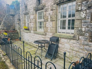 A stone patio with metal table and folded chairs outside a stone building with white windows at 1 Boarbank Farm in Allithwaite near Cartmel