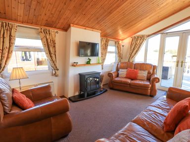 A living room with leather sofas a wall mounted TV and glass doors at Kellet Lodge Lakeside 26 Dock Acres near Carnforth