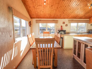 A kitchen dining area with a wooden table and six chairs near windows at Kellet Lodge Lakeside 26 Dock Acres near Carnforth