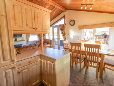 A kitchen area with wooden cabinets next to a dining table with chairs and a living area with leather sofas at Kellet Lodge (Lakeside 26) in Dock Acres near Carnforth