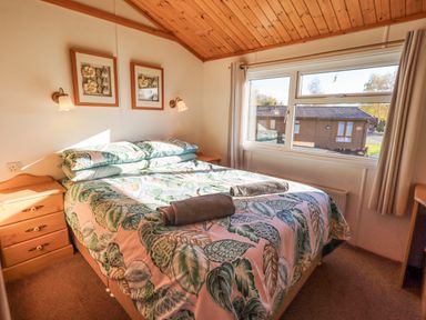 A bedroom with a double bed covered with leaf patterned bedding two towels on the bed wooden ceiling and two framed pictures on the wall at Kellet Lodge Lakeside 26 Dock Acres near Carnforth