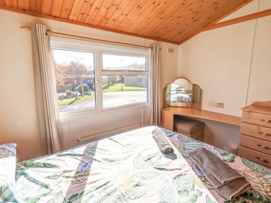 A bedroom with a bed covered in leaf patterned bedding and rolled towels a dressing table with a mirror and a chest of drawers at Kellet Lodge Lakeside 26 Dock Acres near Carnforth