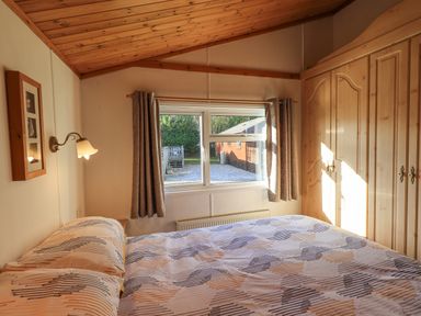 A bedroom with a bed a window with curtains a wall lamp and built in wardrobes at Kellet Lodge Lakeside 26 Dock Acres near Carnforth