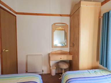 A bedroom with two beds a wooden wardrobe a small dressing table with a round stool and a wall mirror at Kellet Lodge Lakeside 26 in Dock Acres near Carnforth