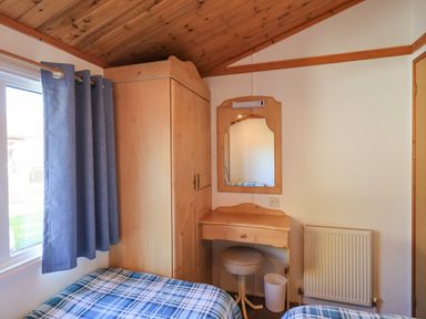 A bedroom with a wooden wardrobe a dressing table with mirror two beds and a window with blue curtains at Kellet Lodge Lakeside 26 Dock Acres near Carnforth