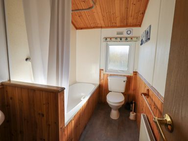 A bathroom with a bathtub shower and toilet with a window above at Kellet Lodge Lakeside 26 Dock Acres near Carnforth