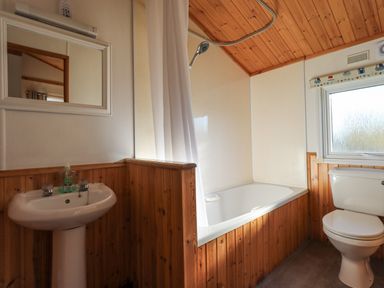 A bathroom with a pedestal sink mirror bathtub shower curtain toilet and frosted window at Kellet Lodge Lakeside 26 Dock Acres near Carnforth