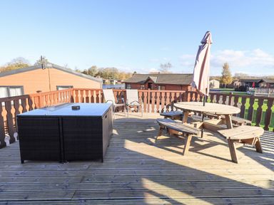 A wooden deck with a round picnic table and umbrella a glass table with stools and two chairs on a raised platform at Kellet Lodge Lakeside 26 Dock Acres near Carnforth