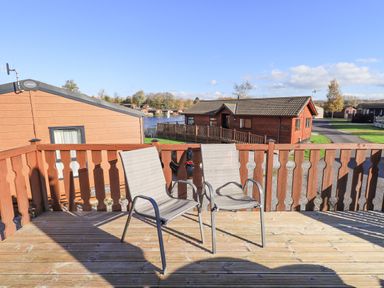 Two chairs on a wooden balcony overlooking lodges and a lake at Kellet Lodge Lakeside 26 Dock Acres near Carnforth