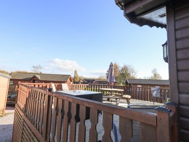 A wooden deck with patio furniture and umbrella overlooking cabins at Kellet Lodge Lakeside 26 Dock Acres near Carnforth