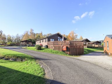 A group of wooden lodges with decking on a grassy area with a paved road at Kellet Lodge Lakeside 26 Dock Acres near Carnforth