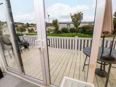 A view of a wooden patio with a round table and umbrella and chairs outside sliding glass doors at 117 Crosswinds Hillway near Bembridge