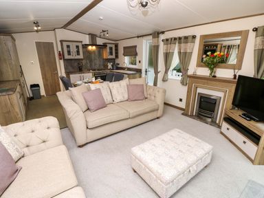 A living room with beige sofas and an ottoman near a fireplace and windows at 117 Crosswinds Hillway near Bembridge