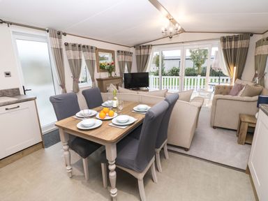 A dining table set with plates glasses and a bottle of wine next to a living area with sofas a TV and large windows at 117 Crosswinds Hillway near Bembridge