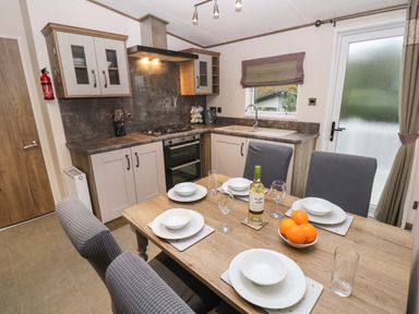 A kitchen with a dining table set with plates glasses a bottle of wine and a bowl of oranges at 117 Crosswinds Hillway near Bembridge