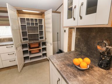 A kitchen with open pantry shelves empty baskets and oranges on the countertop at 117 Crosswinds in Hillway near Bembridge