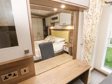 A bedroom with a wooden dressing table and mirror reflecting a double bed with pillows and a yellow headboard at 117 Crosswinds Hillway near Bembridge