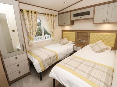 A bedroom with two single beds bedside table wardrobe and window with floral curtains at 117 Crosswinds in Hillway near Bembridge
