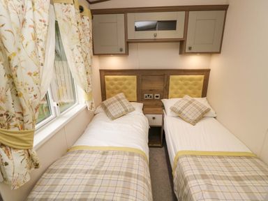 A bedroom with two single beds separated by a nightstand and cabinets above at 117 Crosswinds Hillway near Bembridge