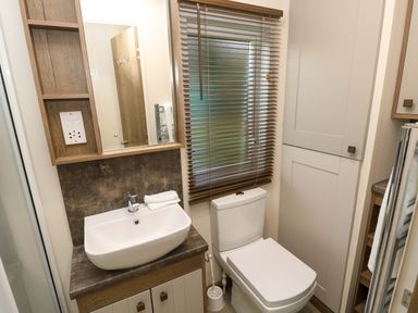 A bathroom with a sink a mirror a toilet a window with blinds and cabinets at 117 Crosswinds in Hillway near Bembridge