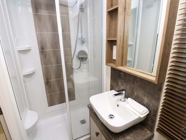 A bathroom with a shower enclosure a sink with a folded towel and a wooden cabinet with a mirror at 117 Crosswinds Hillway near Bembridge
