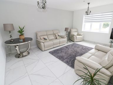 A living room with beige leather sofas a gray rug round table with a plant and lamps at Golygfa Hafan in Little Haven