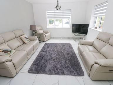 A living room with beige leather sofas armchair a gray rug tiled floor and a TV on a glass stand at Golygfa Hafan in Little Haven