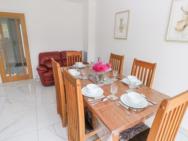 A dining room with a wooden table set for six and a red sofa in the corner at Golygfa Hafan in Little Haven