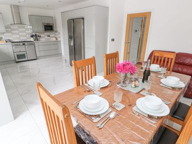 A kitchen with gray cabinets and stainless steel appliances and a dining area with a wooden table set for six and wooden chairs at Golygfa Hafan in Little Haven