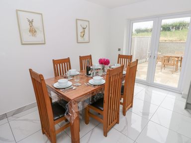A dining room with a wooden table set for six next to glass doors leading to a patio at Golygfa Hafan in Little Haven