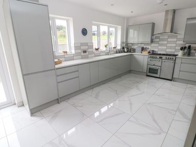 A kitchen with grey cabinets a stainless steel oven and white tiled floor at Golygfa Hafan in Little Haven