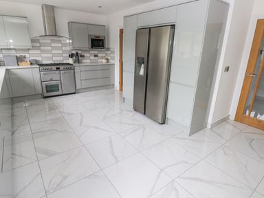 A kitchen with gray cabinets a stainless steel refrigerator a gas stove and oven and white tiled floor at Golygfa Hafan in Little Haven