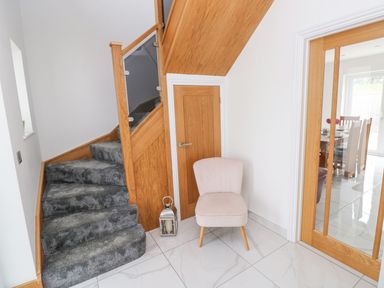 A carpeted staircase with wooden glass balustrade a small wooden door a light pink chair and glass sliding wooden doors in a hallway at Golygfa Hafan in Little Haven