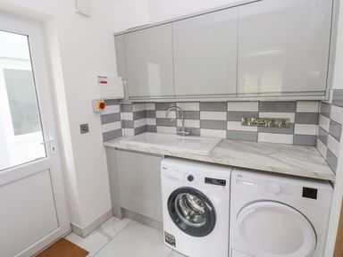 A laundry room with washing machine dryer sink and cabinets at Golygfa Hafan in Little Haven